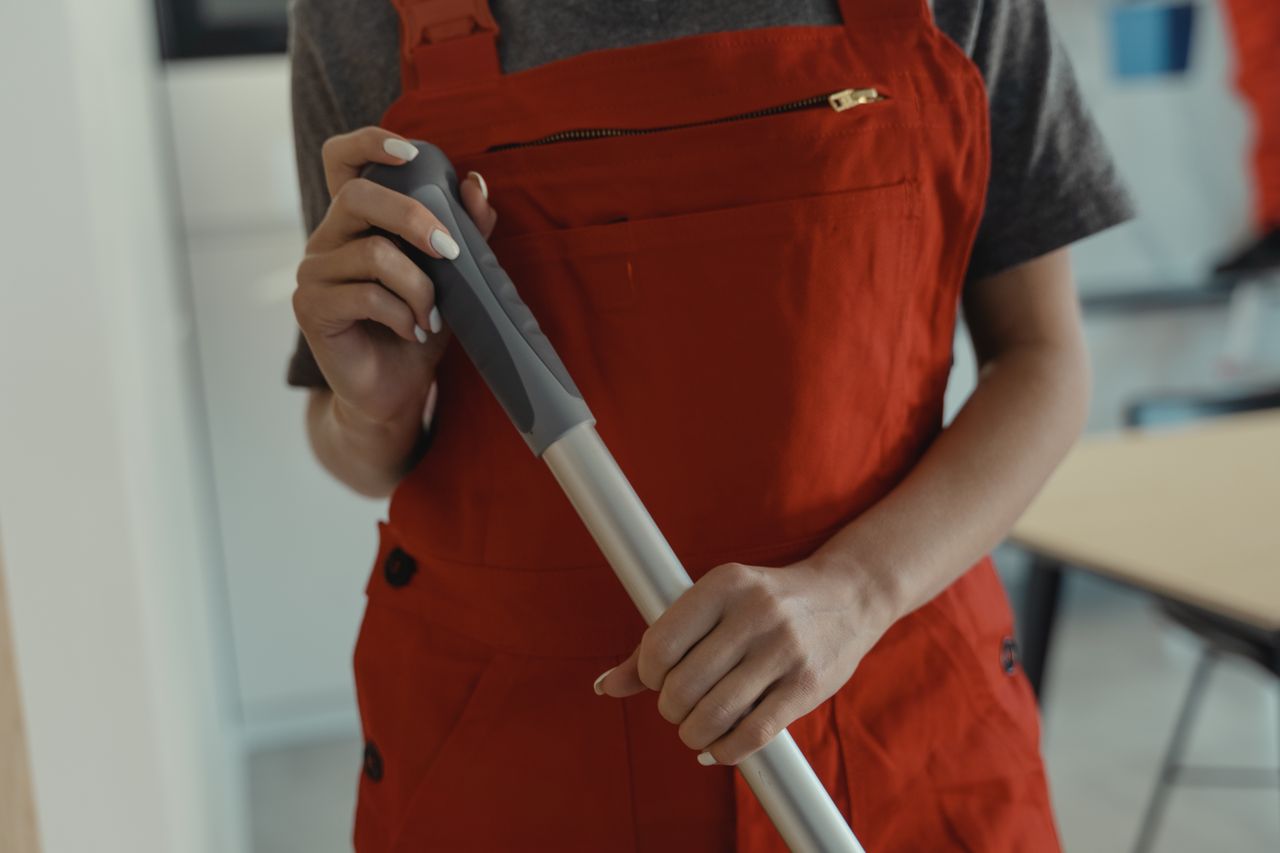 A woman dressed in a red apron holding a mop handle while cleaning indoors.